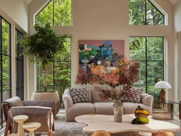 Warm modern living room with tall windows, soft seating, art, and a sculptural coffee table