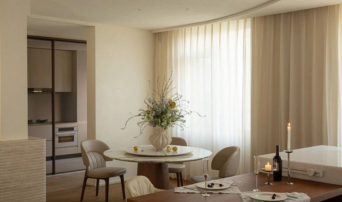 Wide view of living room with cream sofa, teal chair, and sheer curtains at dusk