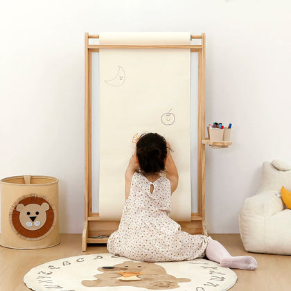  Child drawing on paper supported by a natural wood paper-roll easel; art supplies shown for context