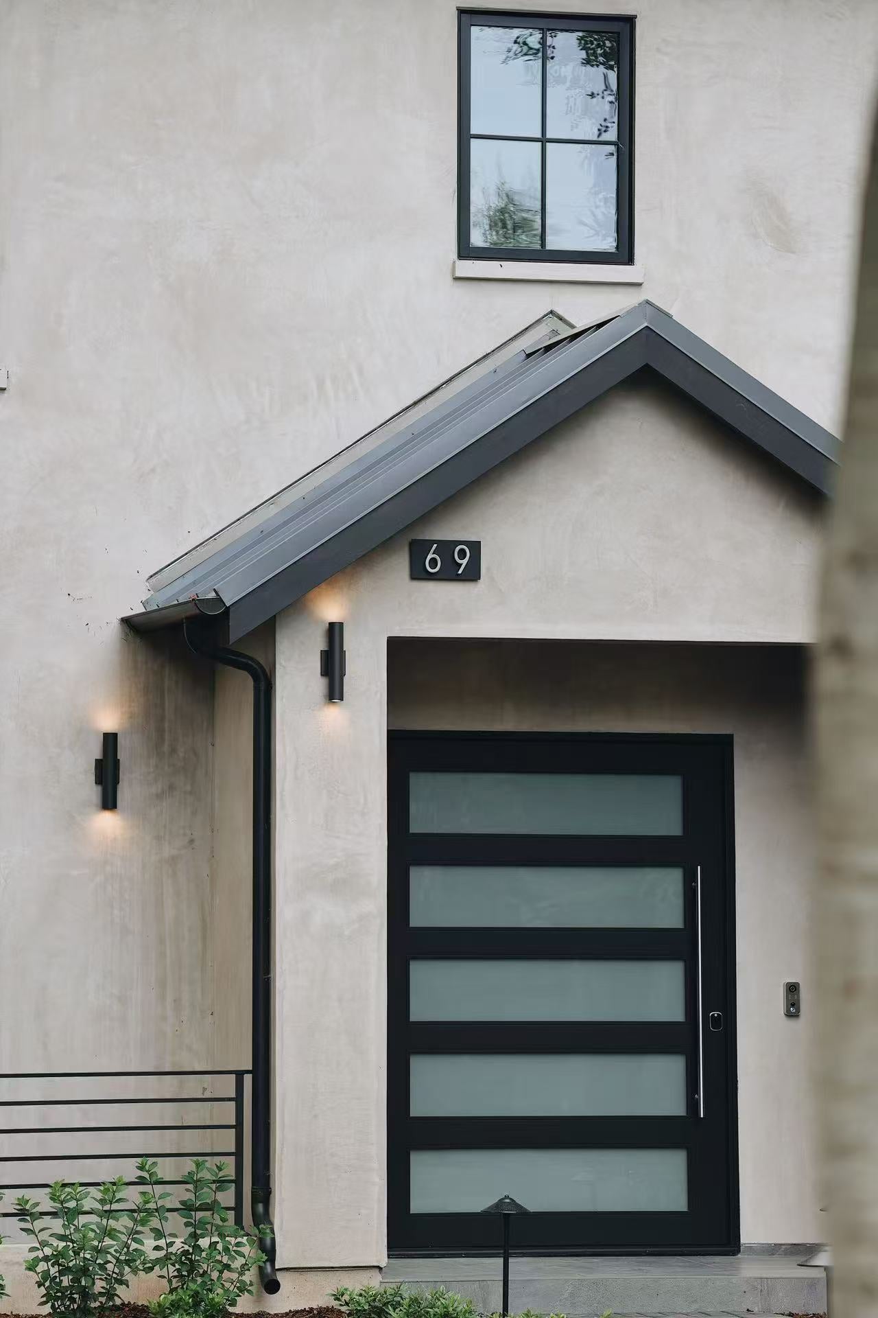 Close view of the entry door with black framing and exterior wall lights