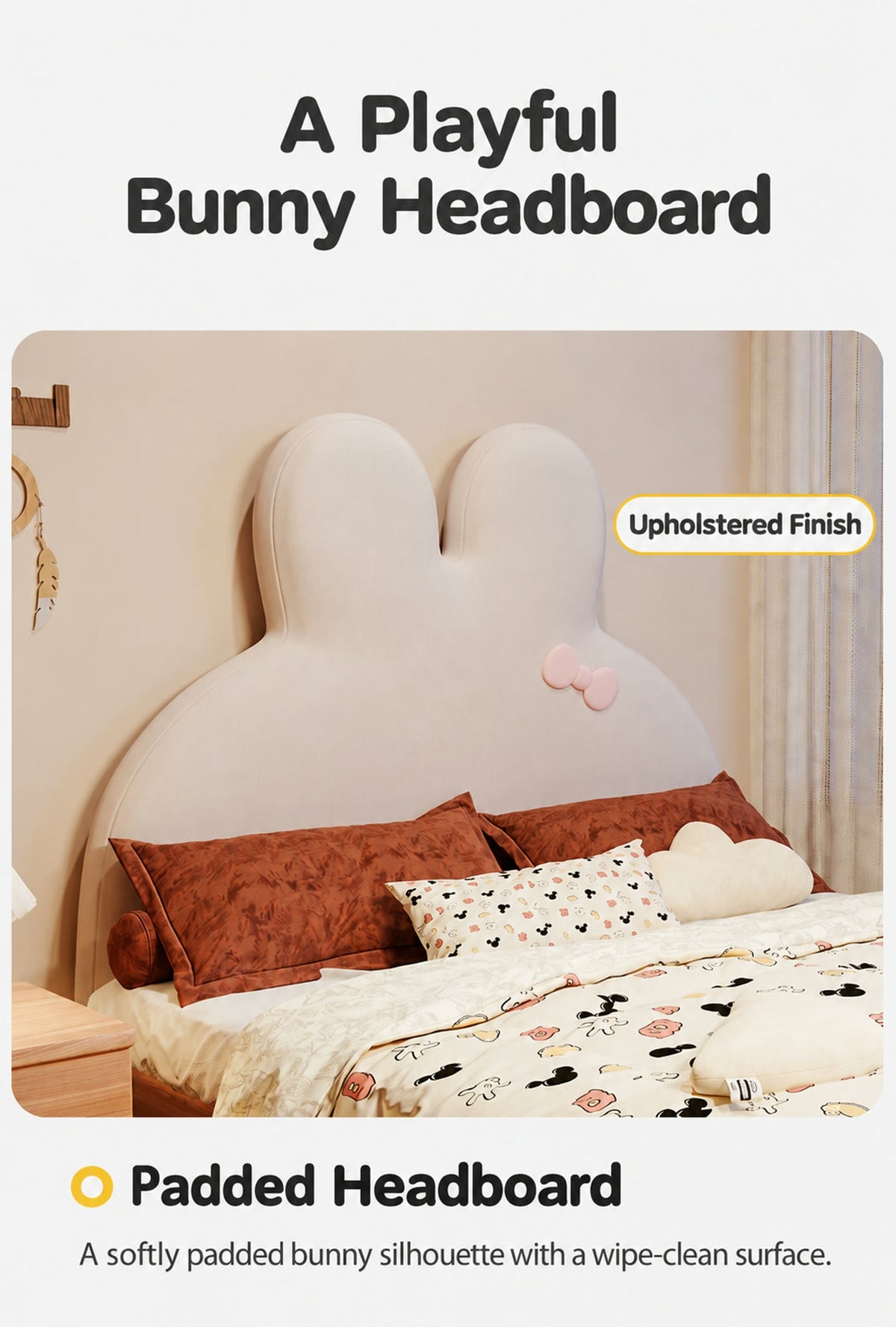  Cream upholstered bunny headboard with rounded ears and pink bow.