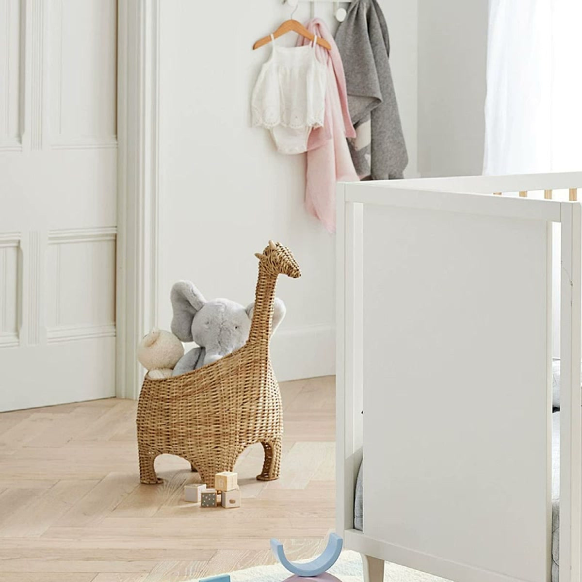  Giraffe basket holding soft toys next to white nursery furniture.