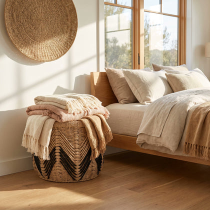  Woven chevron basket holding folded blankets beside a bed.
