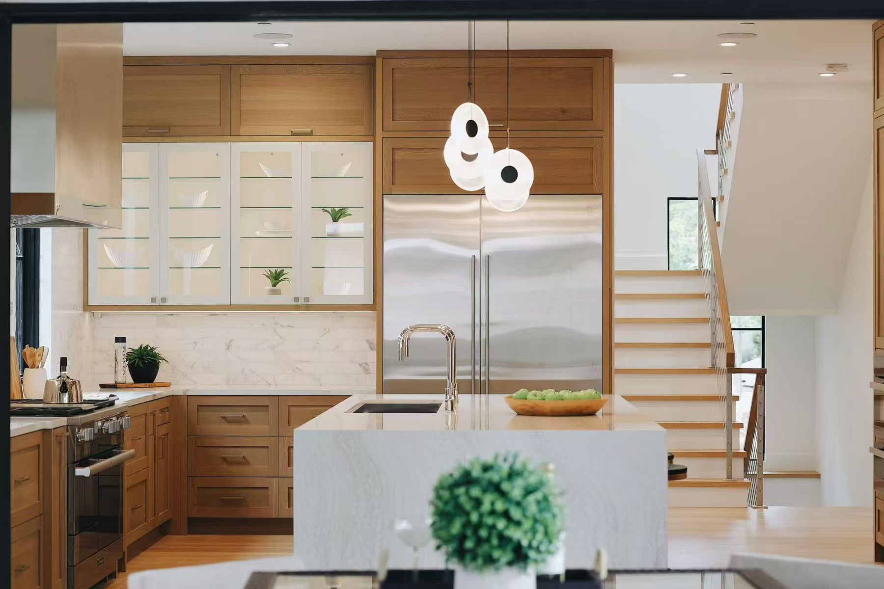 Frontal view of the kitchen island with pendant lights, refrigerator wall, and stair beyond