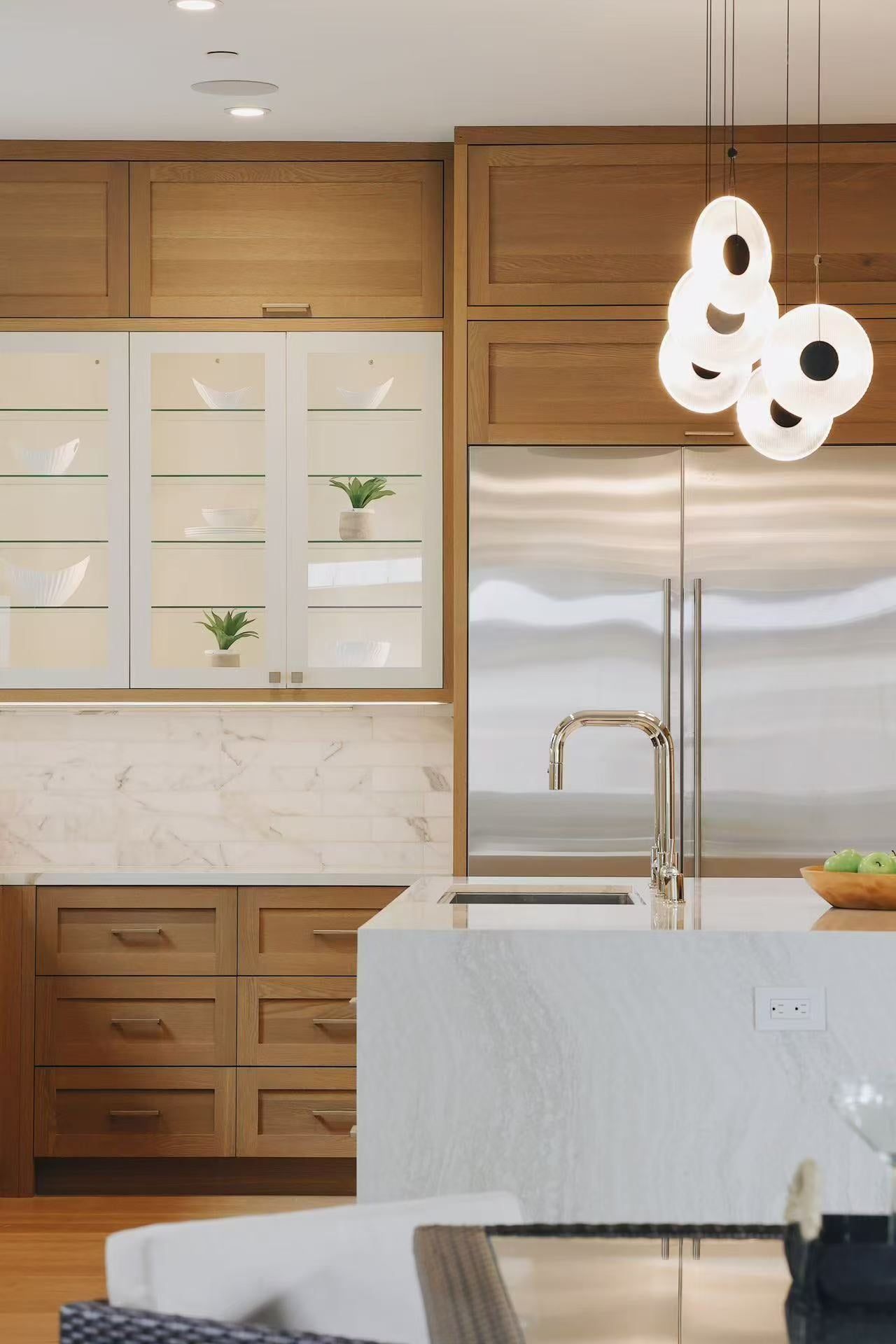 Kitchen island detail with sculptural white pendant lighting and stainless steel refrigerator