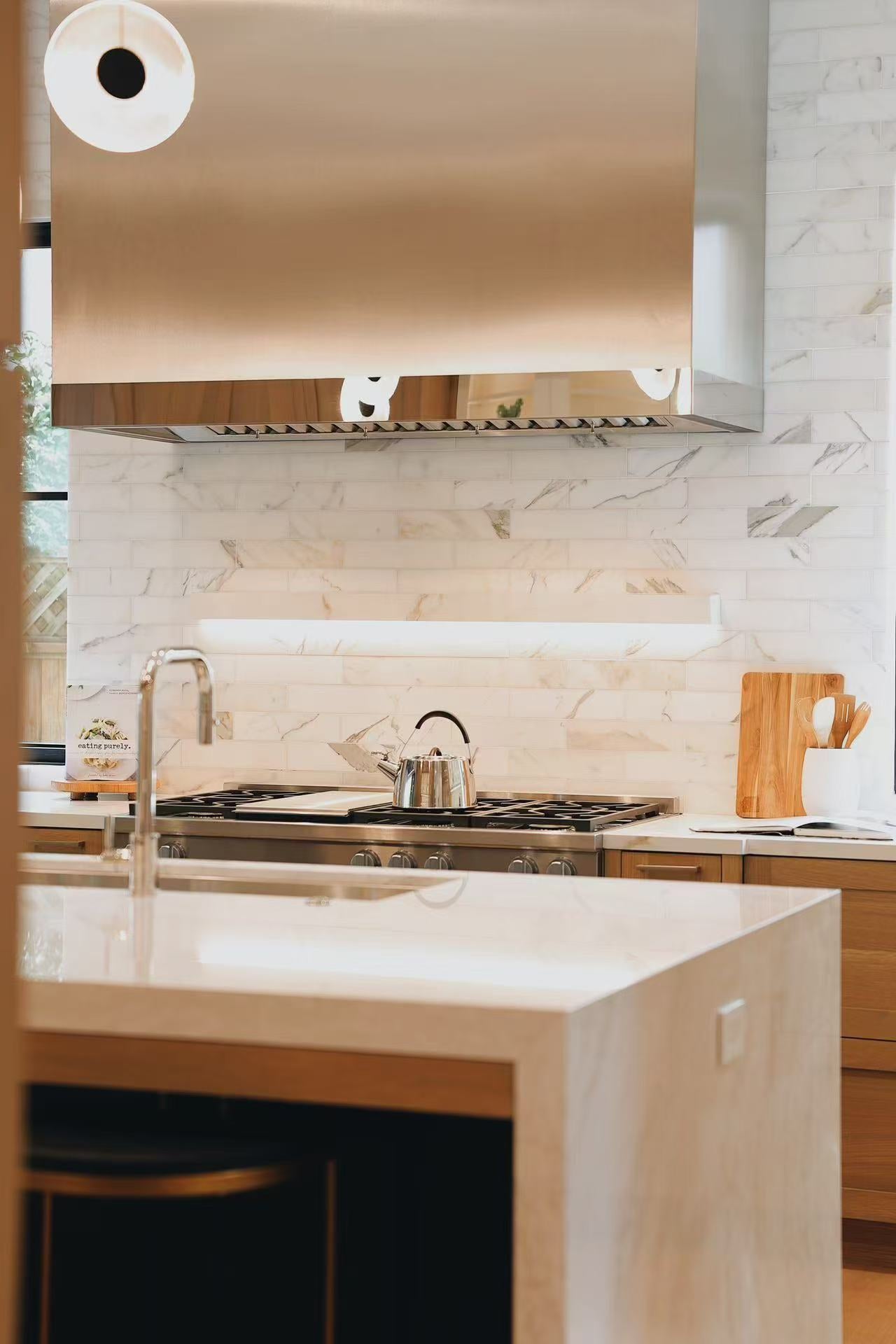 Island side and range wall with stone backsplash and stainless steel hood