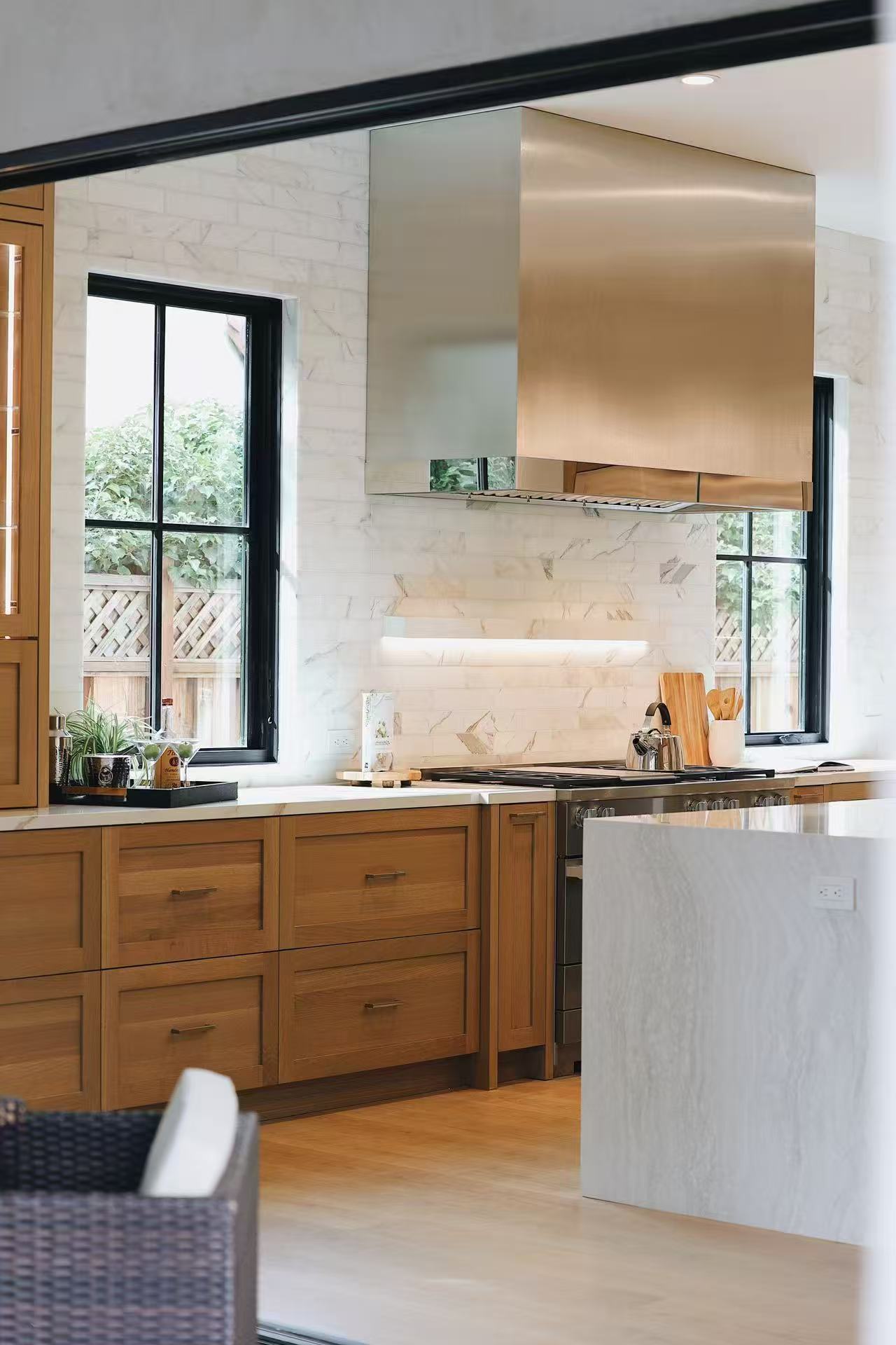 Kitchen threshold view with island, black framing, and warm timber cabinetry