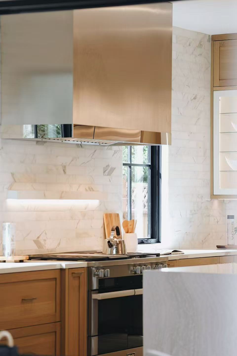 Range wall detail with stainless steel hood, marble-effect backsplash, and timber cabinetry
