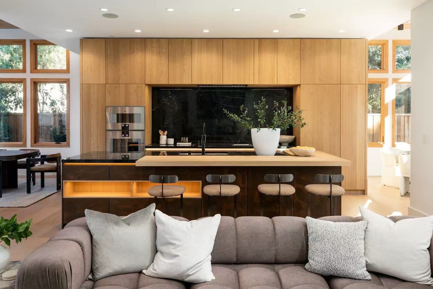 Open living area with warm timber kitchen, black backsplash, island, and soft sectional sofa