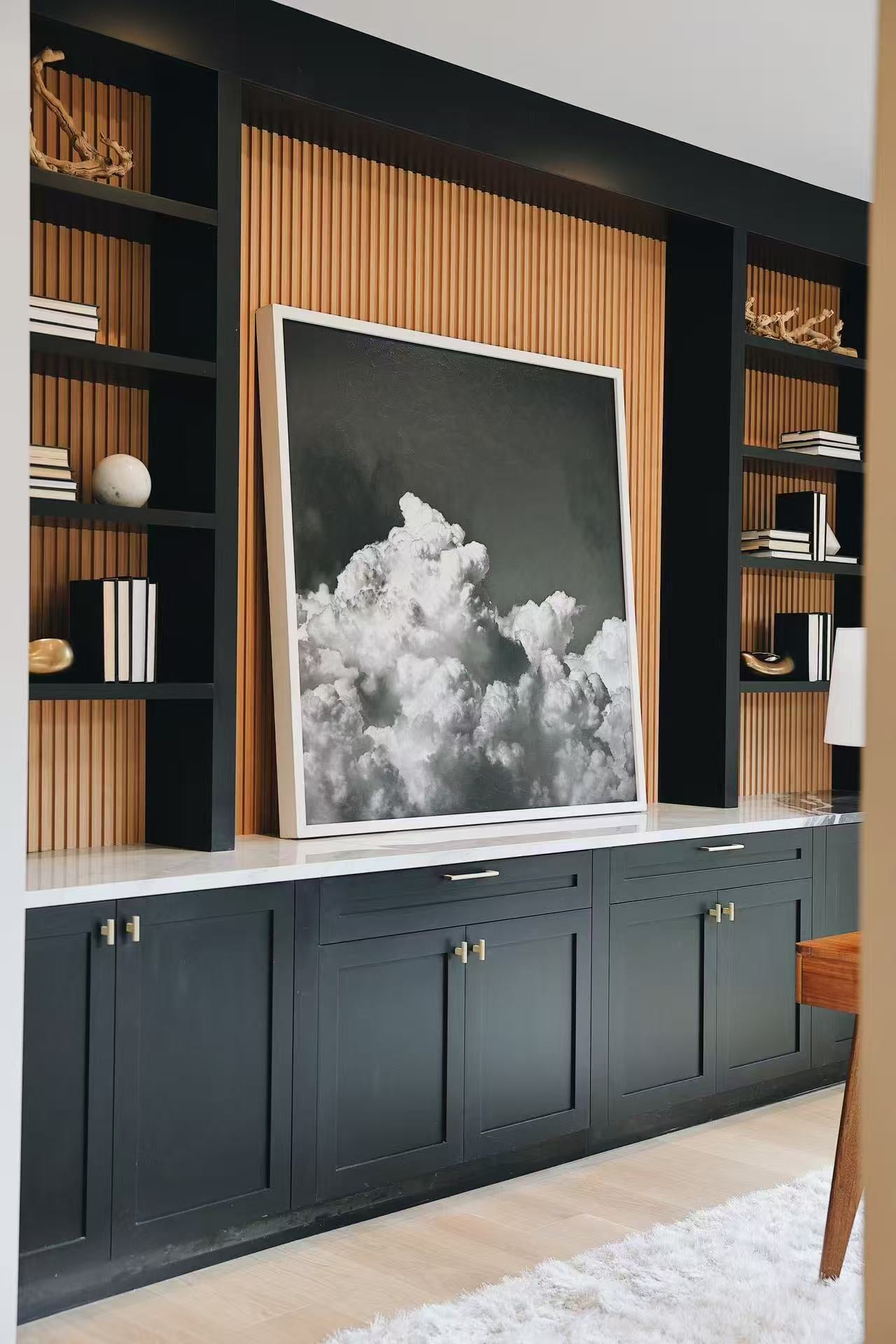 Custom built-in cabinet wall with black cabinetry, warm slatted timber back panel, art, and open shelving