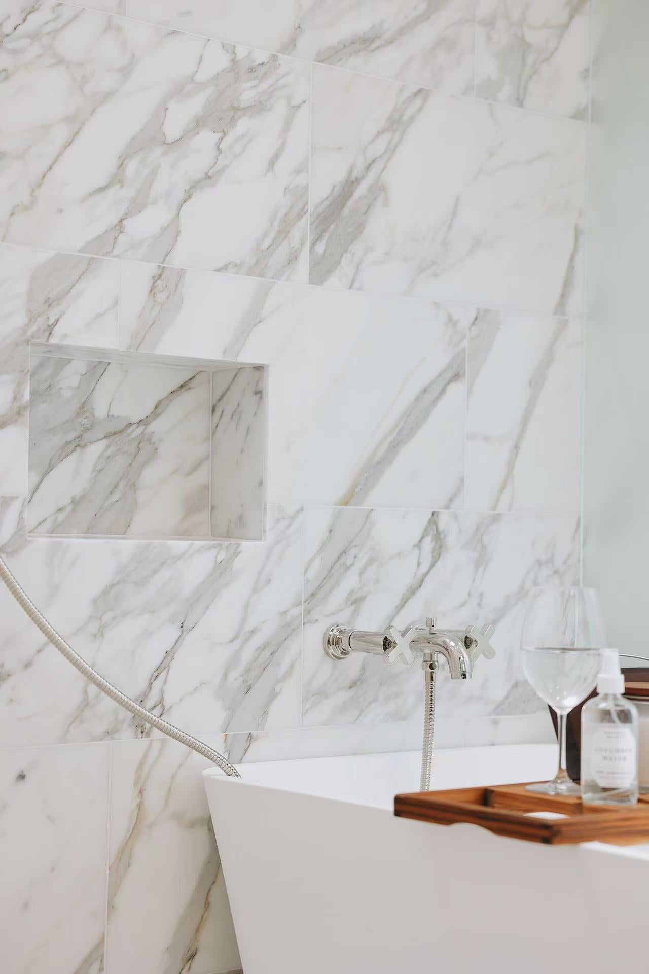 Bathtub area with marble-effect wall tile and wooden bath tray