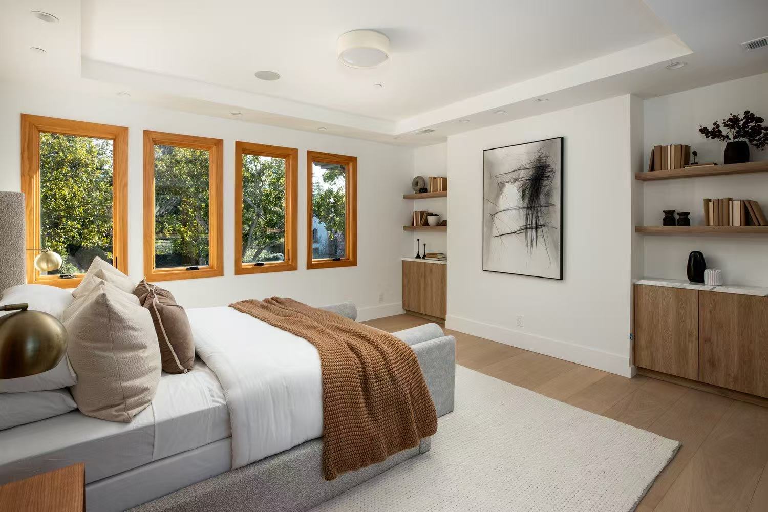 Bedroom with upholstered bed, timber storage, warm throw, and large windows