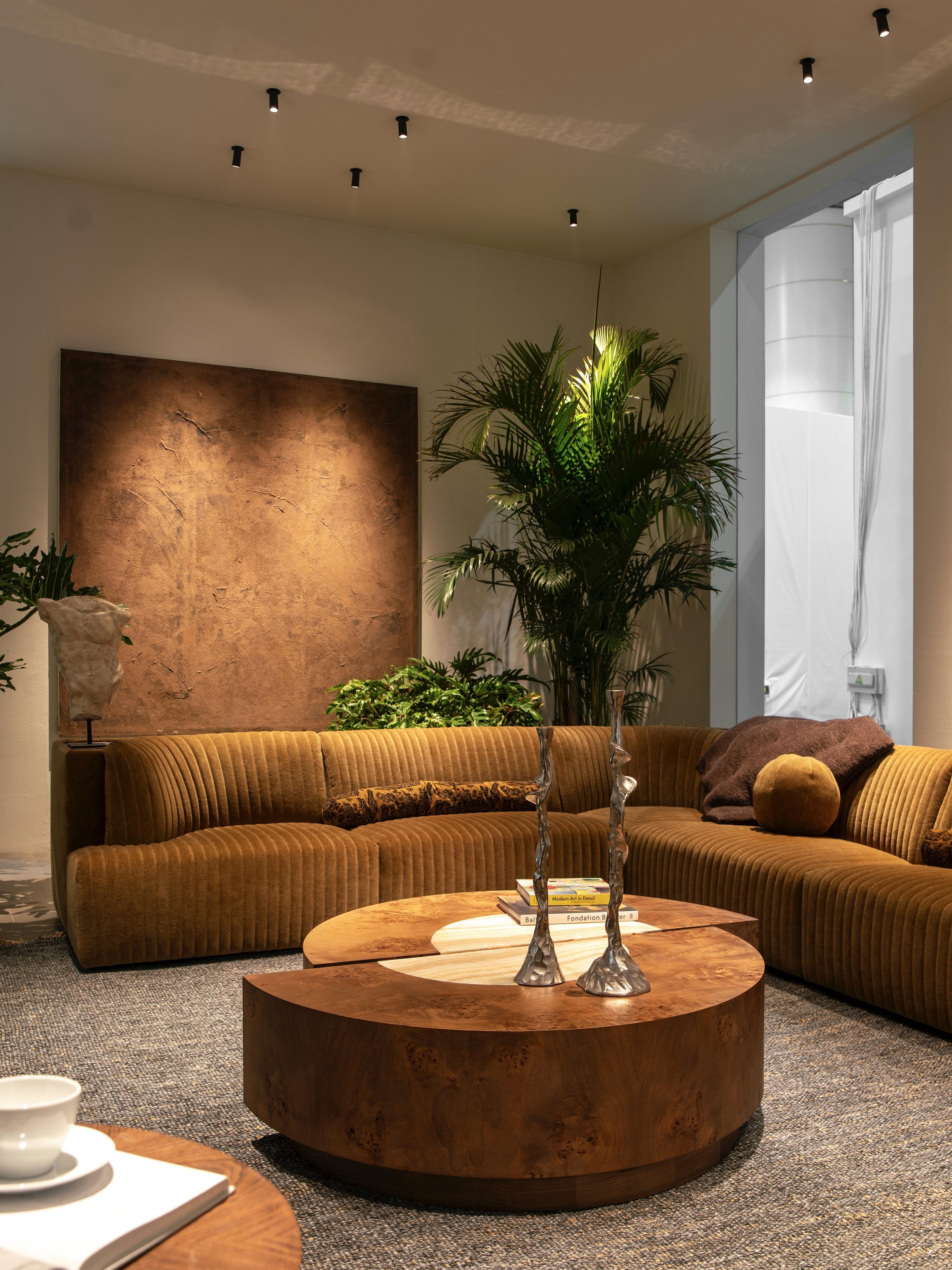 Nature K warm lounge room with textured sofa, round wood table, and indoor greenery