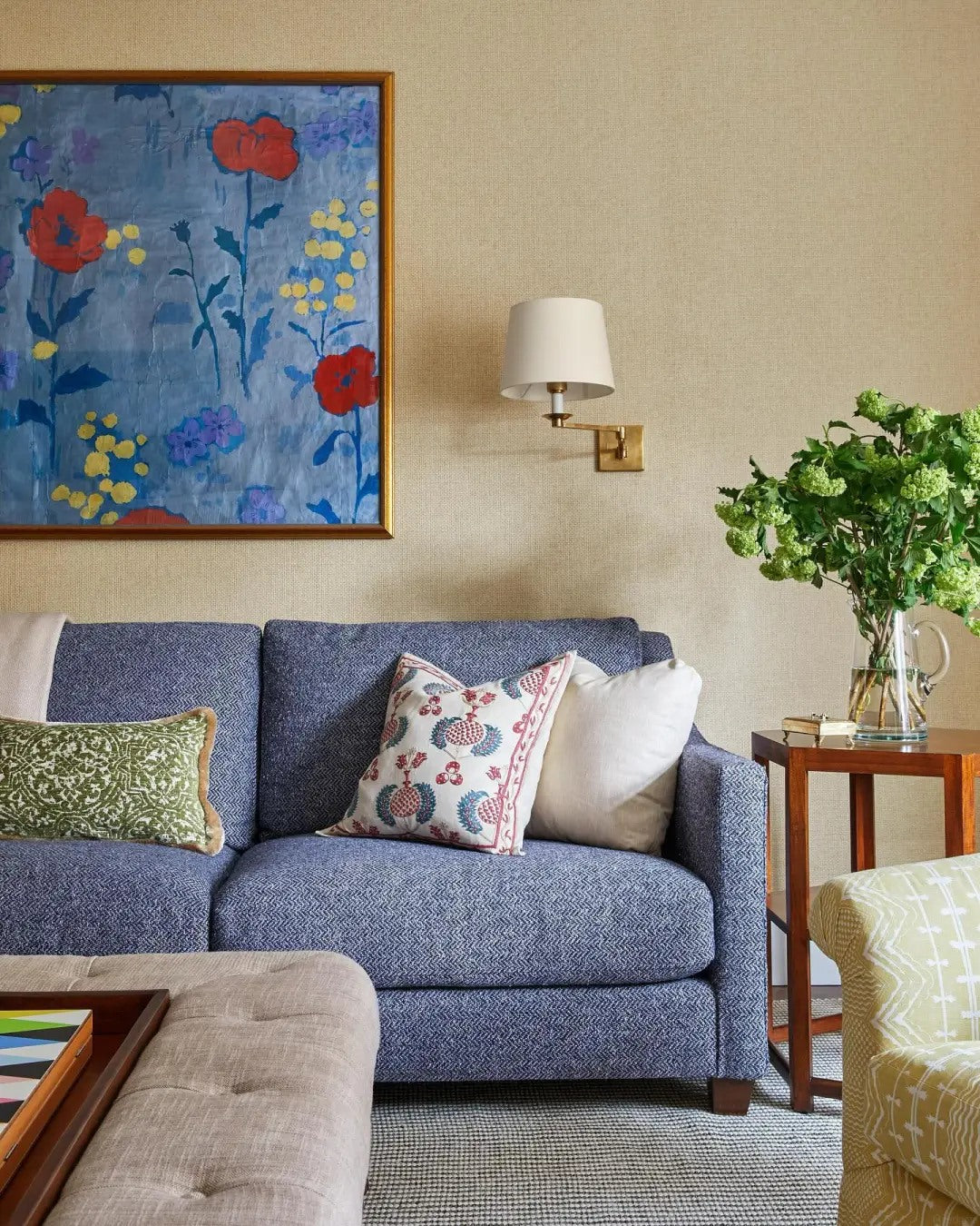 A blue sofa becomes softer with botanical art and warm side lighting.