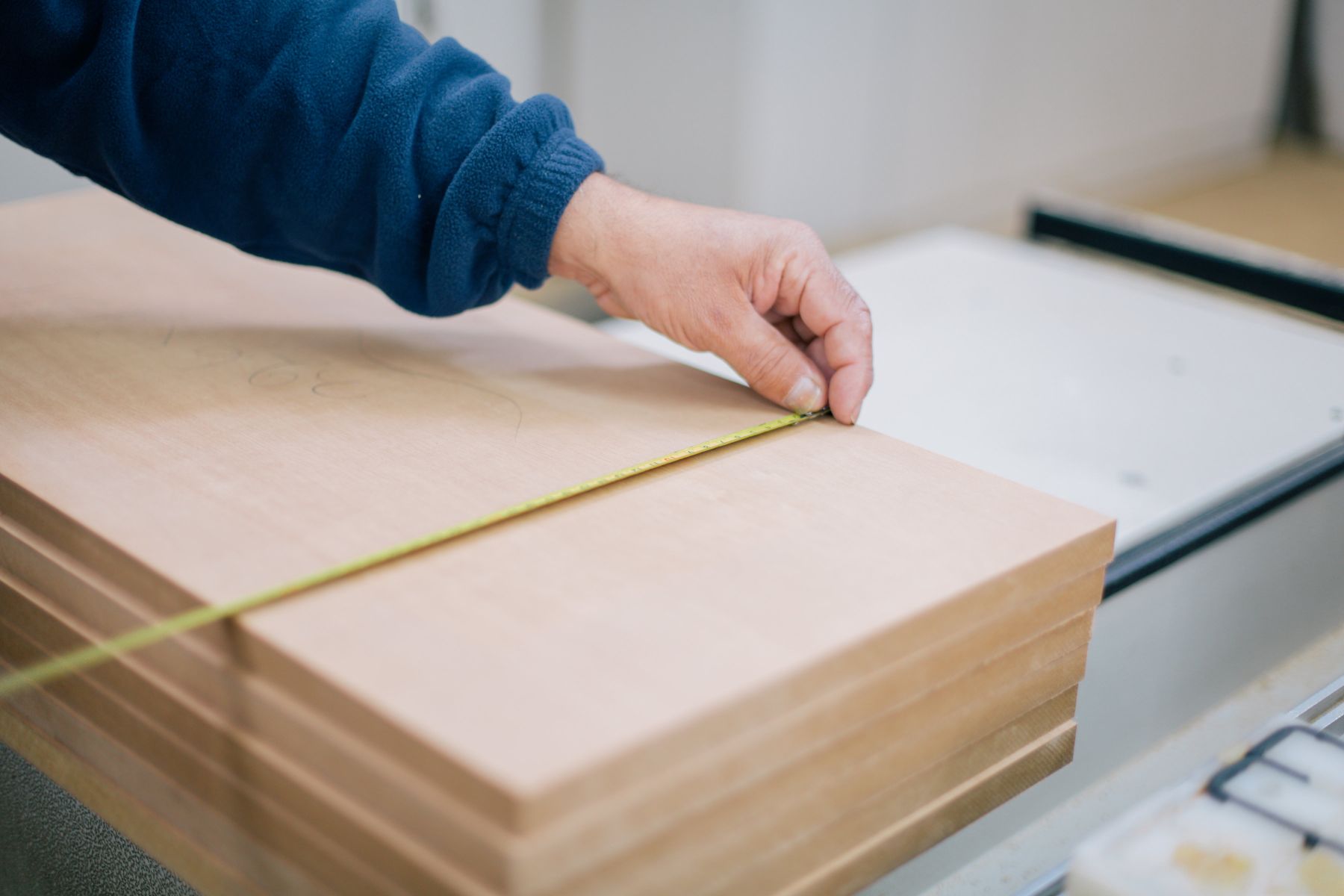 Close-up of a worker checking the width of stacked wood panels with a tape measure