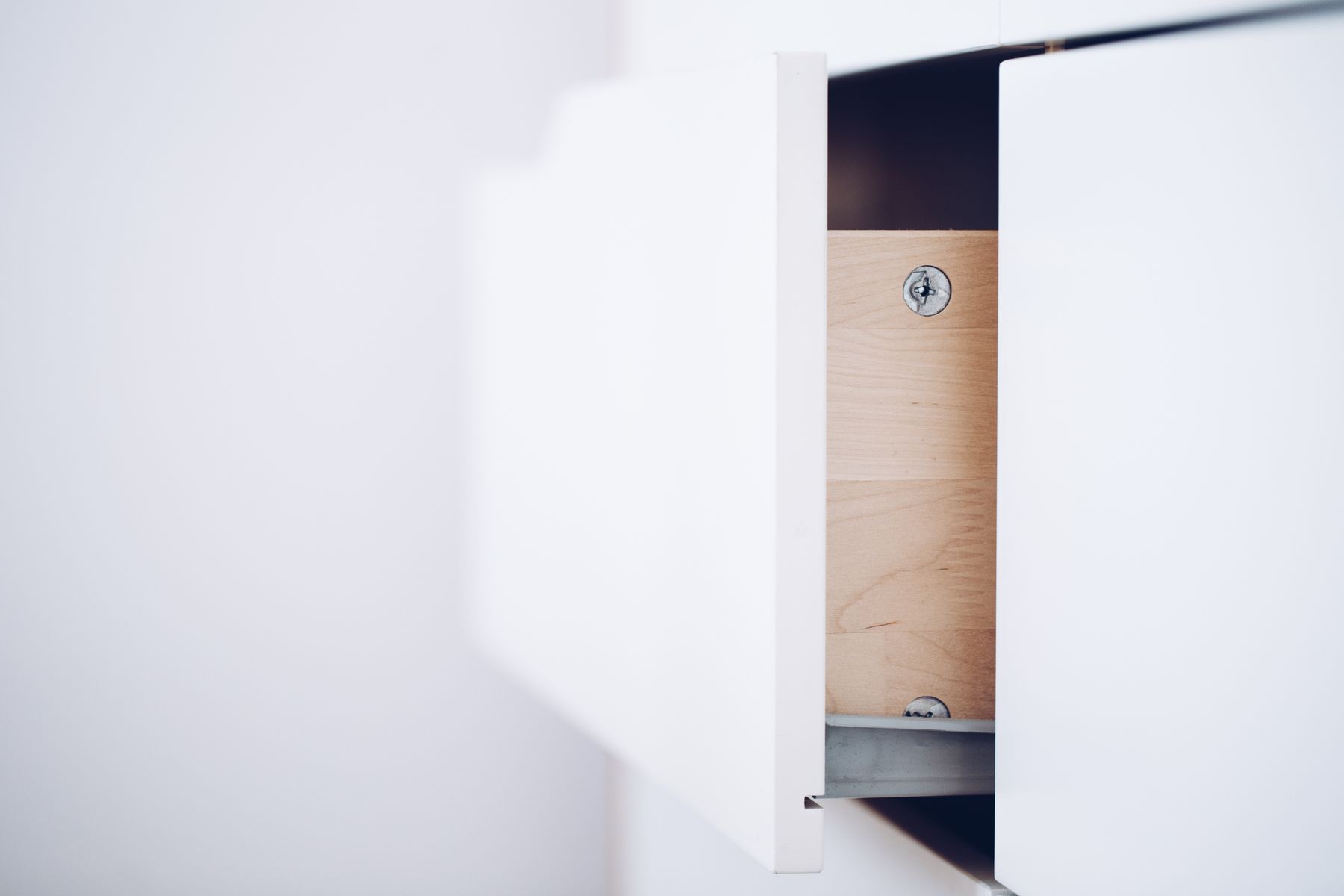 Partially open white drawer showing its wood interior, fixings and metal runner