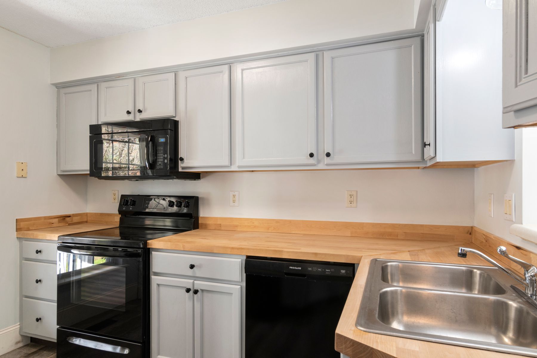White kitchen cabinetry coordinated with an oven, microwave, dishwasher and sink