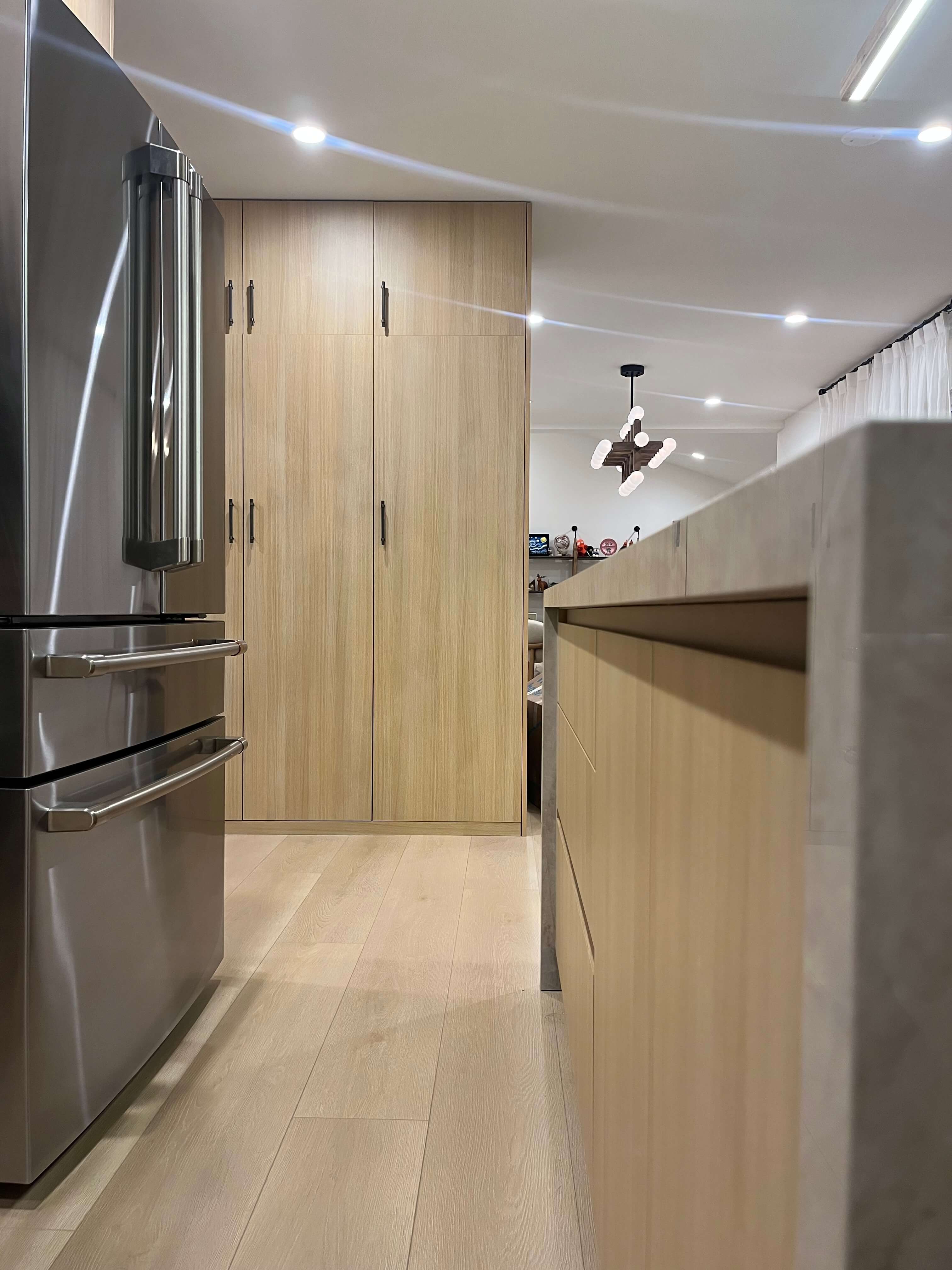 Looking down the kitchen past the refrigerator to the tall pantry doors