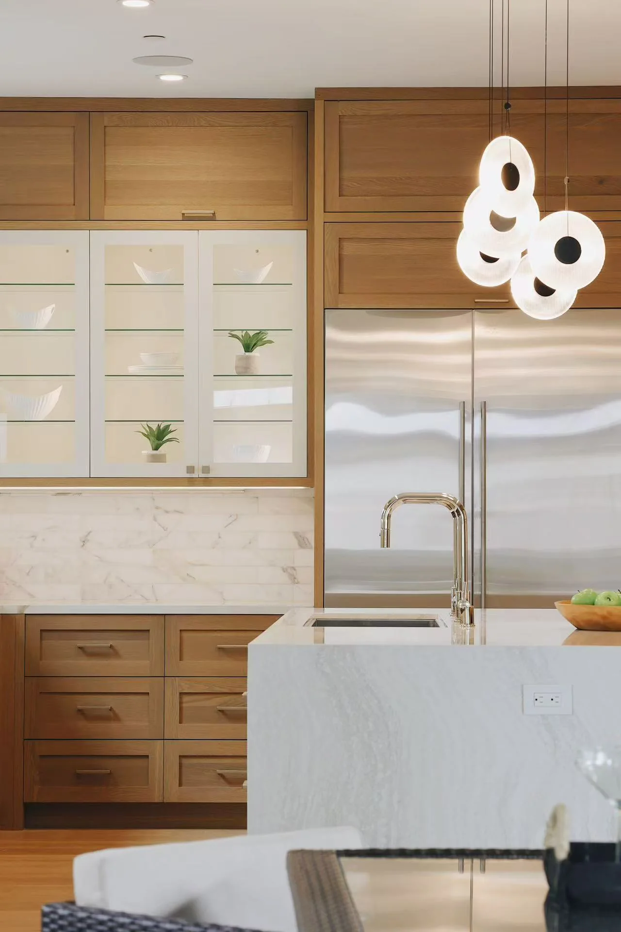 Kitchen island detail with sculptural white pendant lighting and stainless steel refrigerator