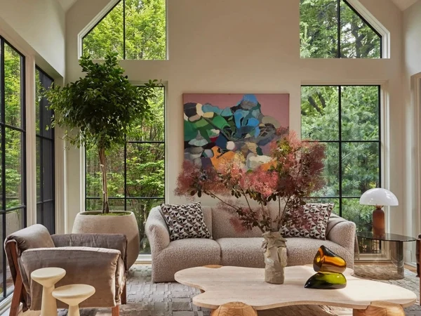 Warm modern living room with tall windows, soft seating, art, and a sculptural coffee table