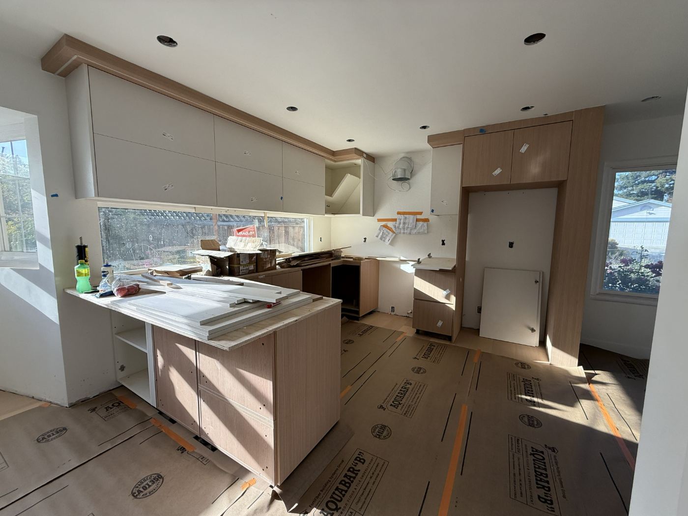 Kitchen during installation with upper cabinets hung, oak base run in place and the floor covered