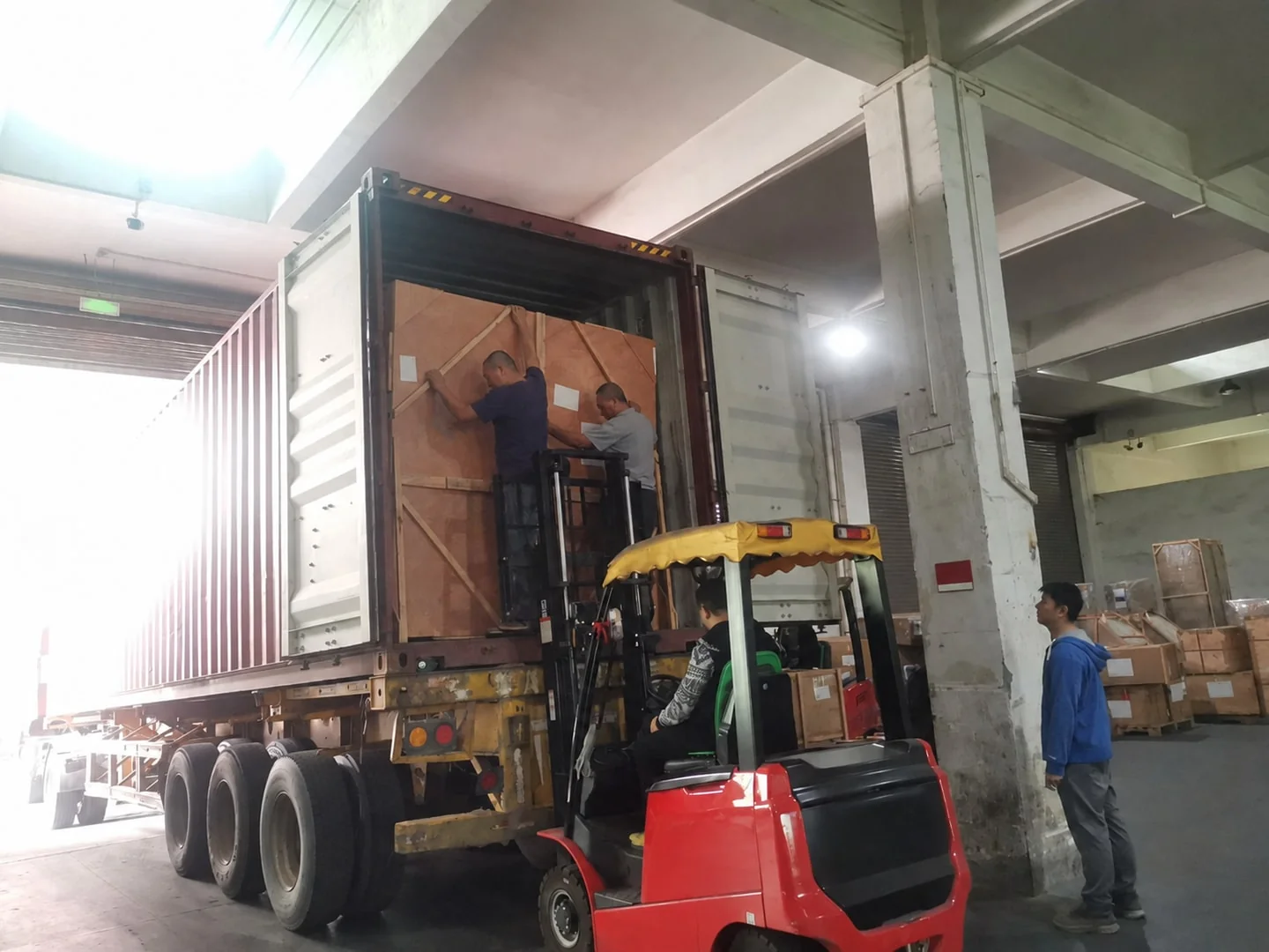 Workers loading wood-crated furniture into a shipping container with a forklift